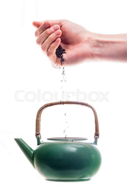 Hand pouring tea leaves into the green ceramic teapot, stock photo