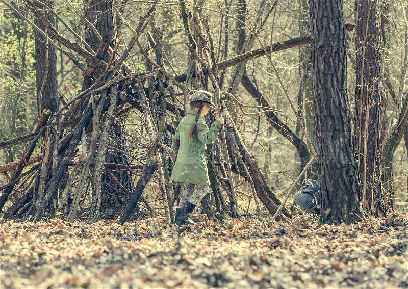 Ittle cute girl builds a hut in the woods. back view. Photo in retro style, stock photo