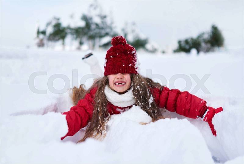 Girl fell into the snow and laughing, hat covering her eyes, stock photo