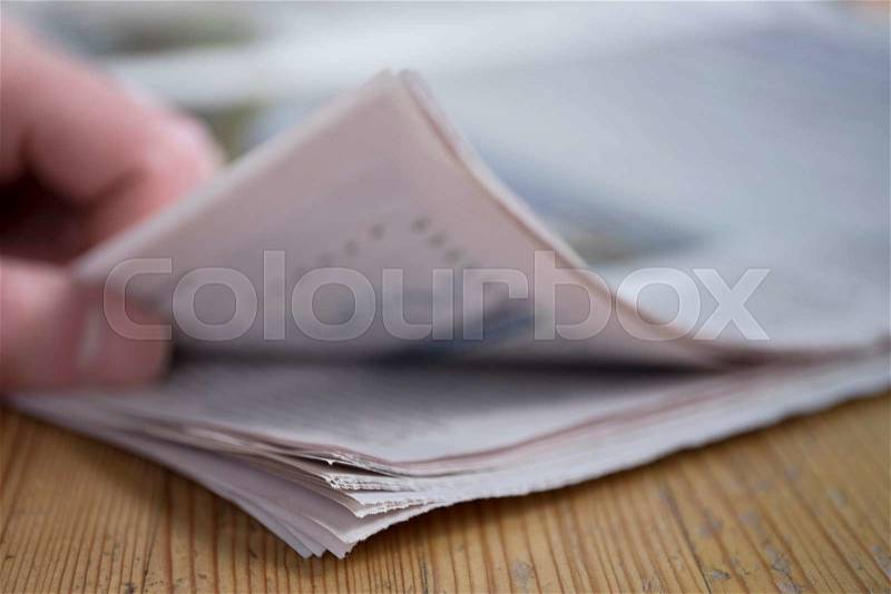 Man turning a page of a newspaper on a wooden table, focus on paper, stock photo