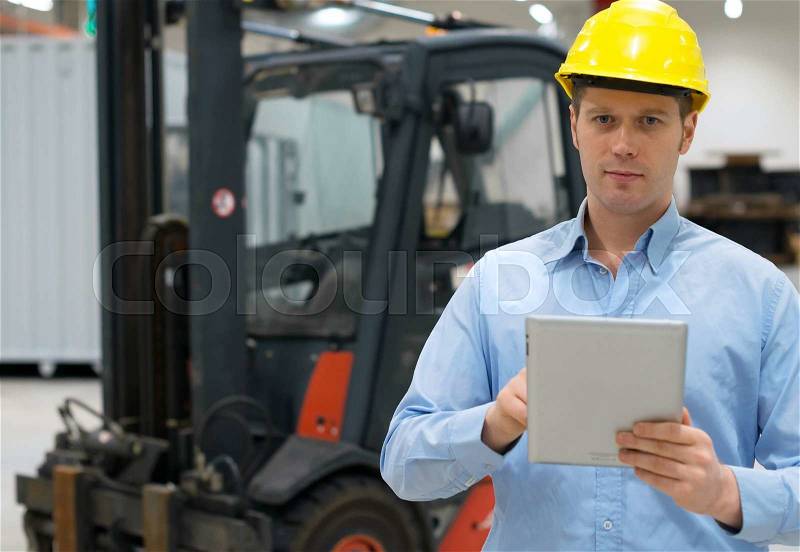 Warehouseman in hard hat with tablet pc at warehouse, stock photo