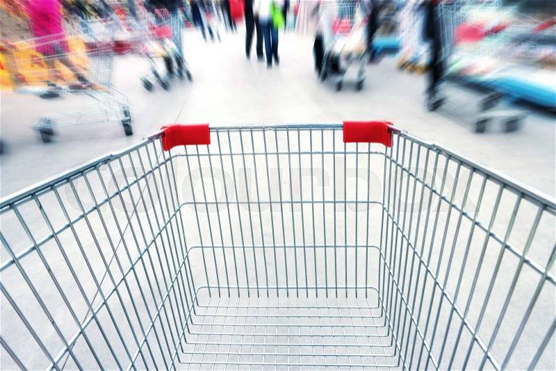 Empty trolley in supermarket or mall full of crowded people. Blur motion, stock photo