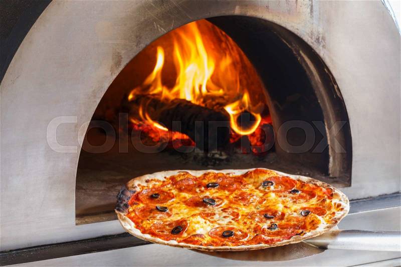 Close up pizza in firewood oven with flame behind, stock photo