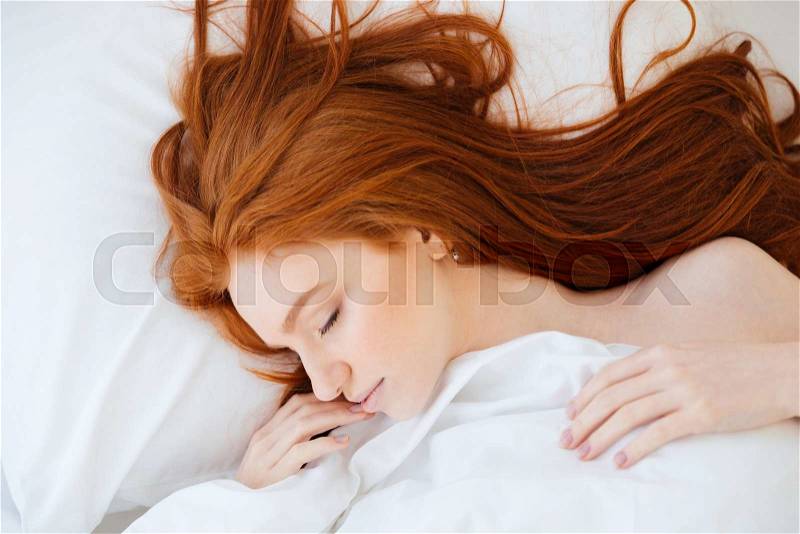 Tender cute young woman with long red hair lying and sleeping in white bed, stock photo