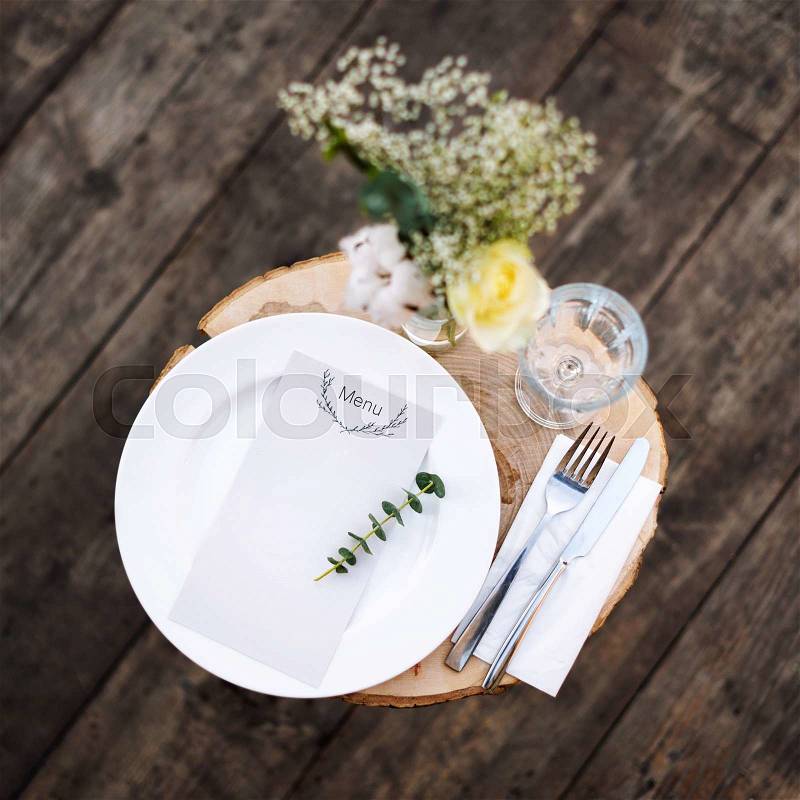 Paper menu on decorated table ready for dinner. Beautifully decorated table set with flowers, plates and serviettes for outdoor wedding ceremony or another event in the restaurant, stock photo