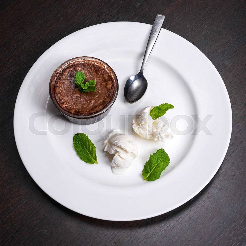 Warm dessert chocolate fondant lava cake served with vanilla ice cream balls and mint on white plate. Famous French dessert on dark wooden table top view, stock photo