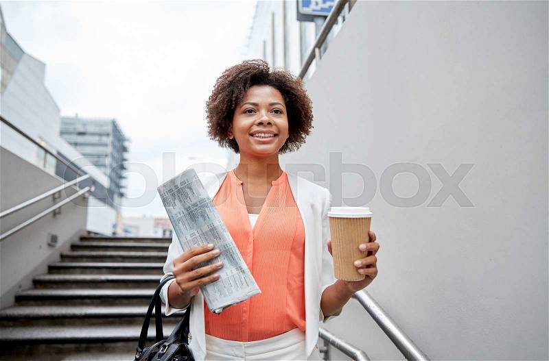 Business and people concept - young smiling african american businesswoman with coffee cup going down stairs into city underpass, stock photo