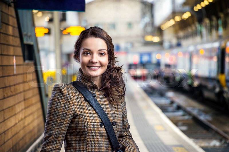 Young woman in checked brown winter coat waiting on train station, stock photo