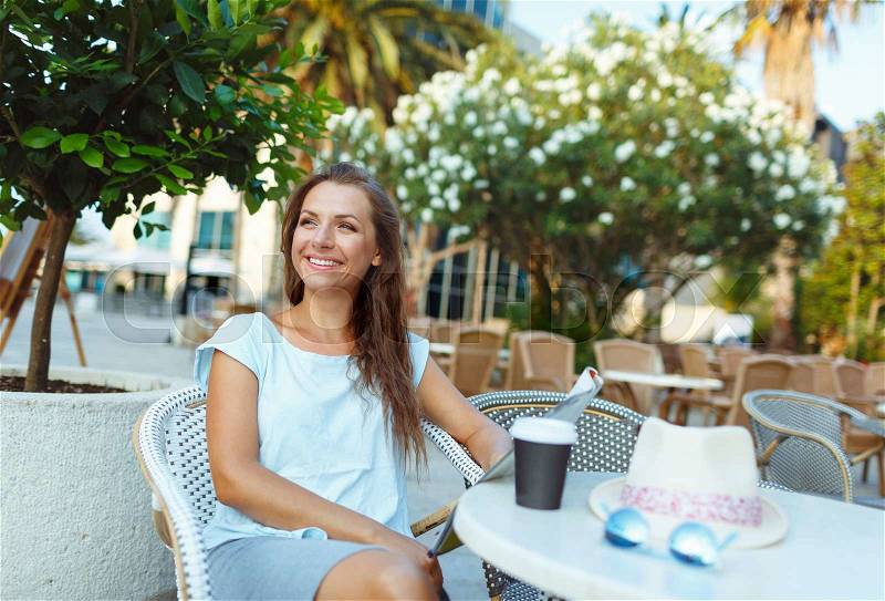 Young woman relaxing in the outdoor cafe - drinking coffee and reading the newspaper, stock photo