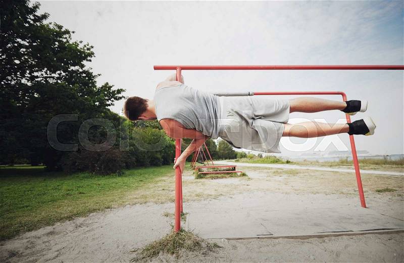 Fitness, sport, training and lifestyle concept - young man exercising on parallel bars outdoors, stock photo