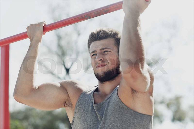 Fitness, sport, exercising, training and lifestyle concept - young man doing pull ups on horizontal bar outdoors, stock photo