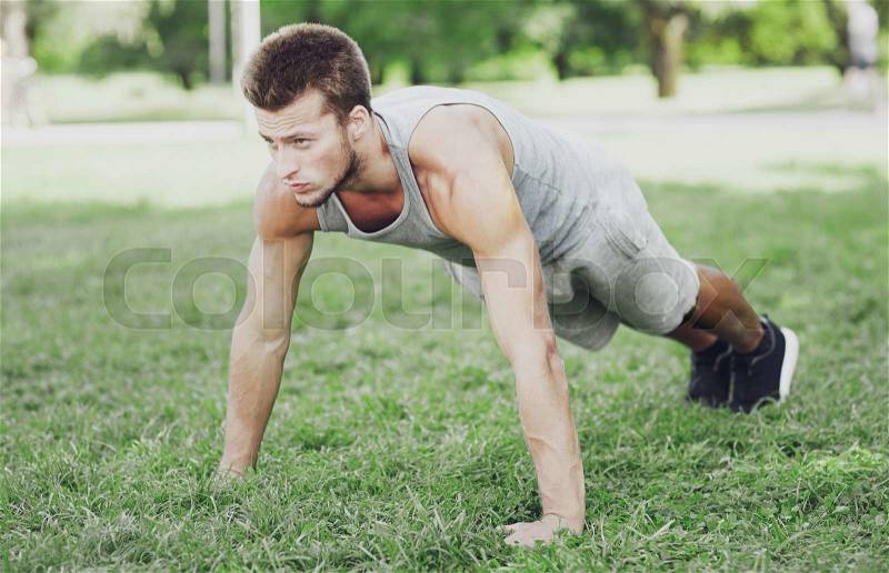 Fitness, sport, exercising, training and lifestyle concept - young man doing push ups or plank exercise on grass in summer park, stock photo