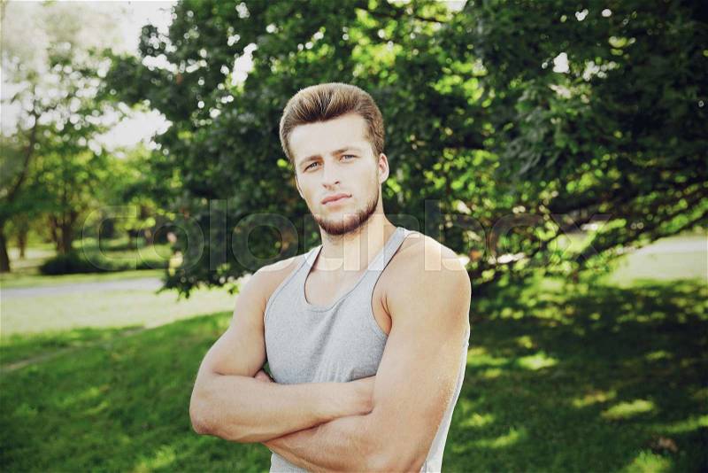 Fitness, sport, people and healthy lifestyle concept - sporty young man with crossed arms at summer park, stock photo