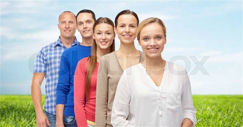 Family, gender and people concept - group of smiling men and women over blue sky and grass background, stock photo