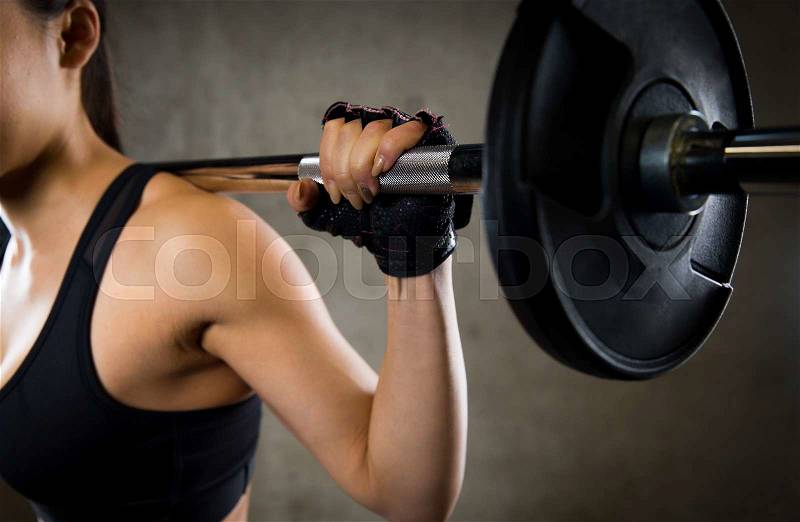 Sport, fitness, bodybuilding, weightlifting and people concept - close up of young woman with barbell flexing muscles in gym, stock photo