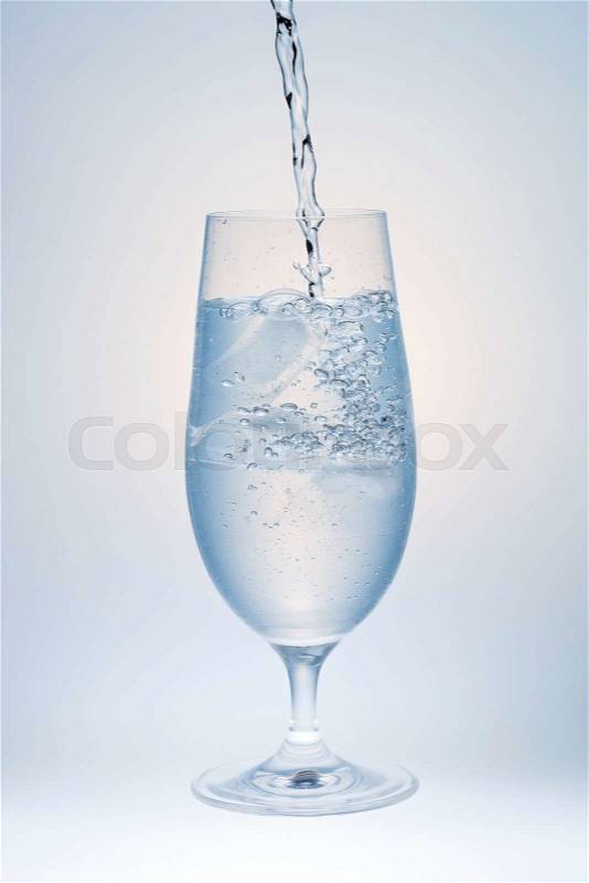 Water Pouring into Glass with Ice on white and grey background, stock photo