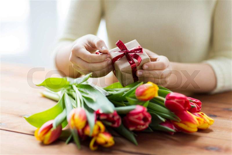 People, holidays and greeting concept - close up of woman holding gift box and tulip flowers, stock photo