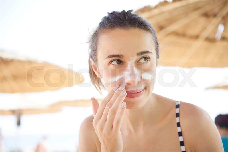 Beautiful woman smears face sunscreen at the beach for protection, stock photo