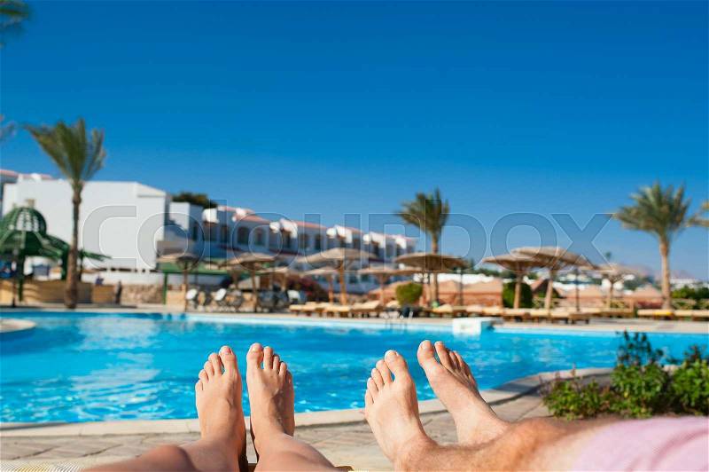 Man and woman sunbathing by the pool at the hotel, stock photo
