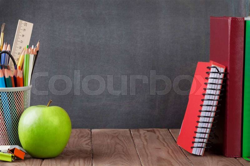 School and office supplies and apple on classroom table in front of blackboard. View with copy space, stock photo