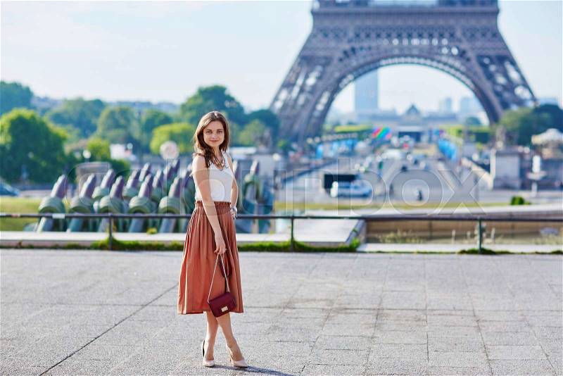 Beautiful young Parisian woman in long brown silk skirt near the Eiffel tower on a summer day, stock photo