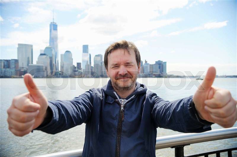 Happy middle age man giving thumbs up sign with Manhattan skyscrapers in New York City , stock photo