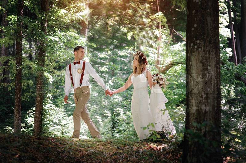 Bride and groom walking on edge of a pine forest on the wedding day, stock photo