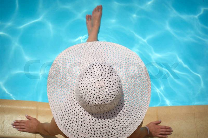 Beautiful woman in a white hat sitting on the edge of the pool, stock photo