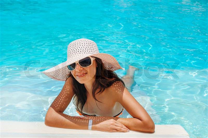 Young beautiful woman in big white hat on edge of the pool, stock photo