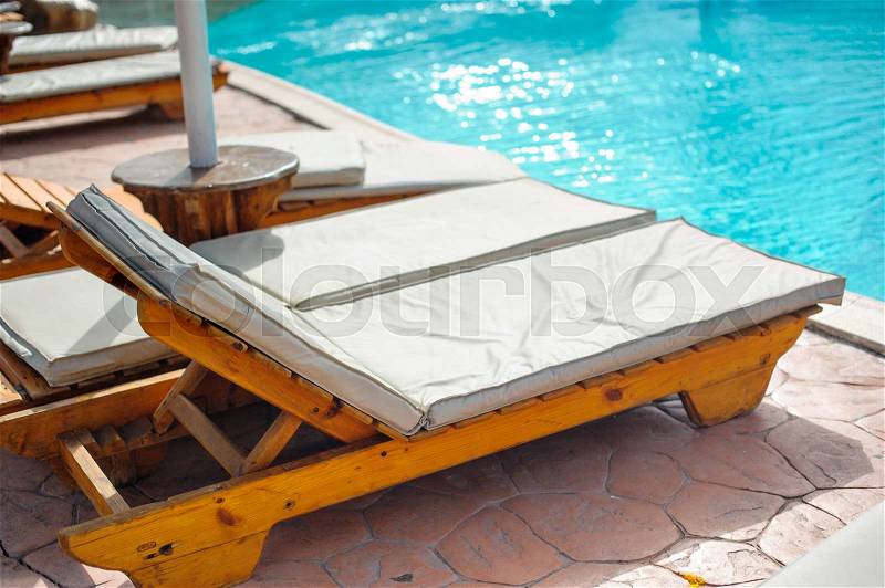 Wooden bed beside the pool. The beds are arranged behind the pool\'s edge, stock photo
