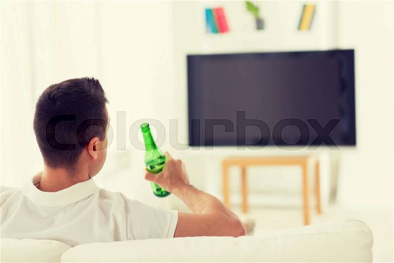 Leisure, technology, mass media and people concept - man watching tv and drinking bottle beer at home from back, stock photo