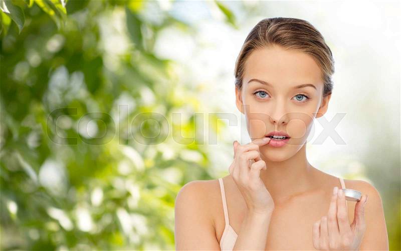 Beauty, people and lip care concept - young woman applying lip balm to her lips over green natural background, stock photo