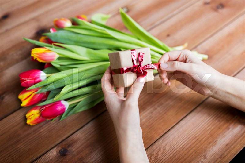 Peoople, holidays and greeting concept - close up of woman holding gift box and tulip flowers, stock photo