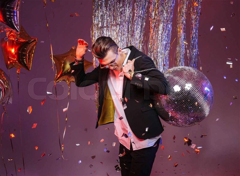 Happy handsome man in sunglasses holding disco ball and dancing alone over purple background, stock photo