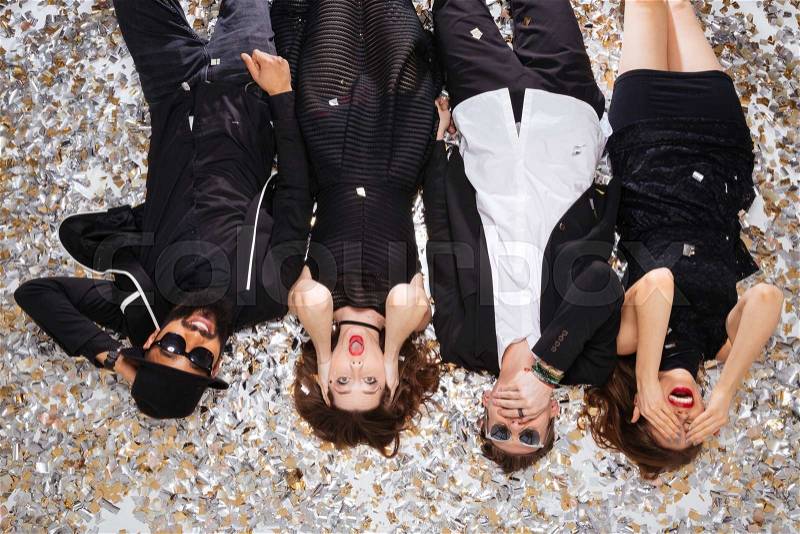 Top view of multiethnic group of funny young friends grimacing and lying on sparkling confetti background, stock photo
