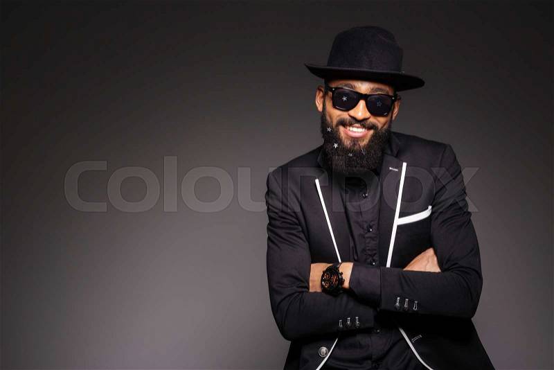 Happy afro american man in fashion cloth standing with arms folded over black background, stock photo