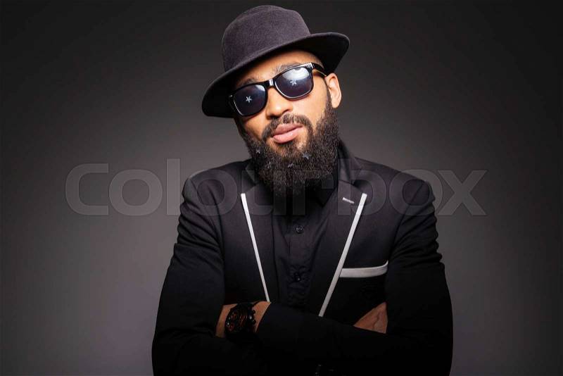 Serious afro american man in fashion cloth and glasses standing with arms folded over black background, stock photo