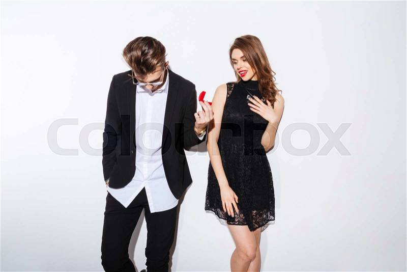 Handsome shy young man giving an engagement ring to his girlfriend over white background, stock photo