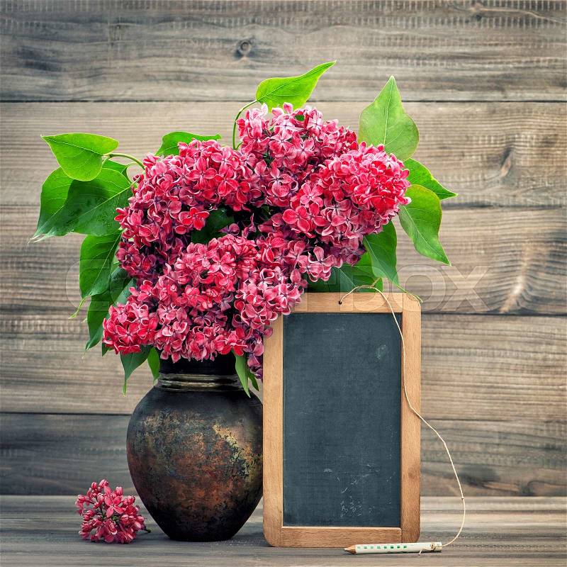 Red flowers in vase on wooden background. Blackboard with space for your text. Retro style toned picture, stock photo
