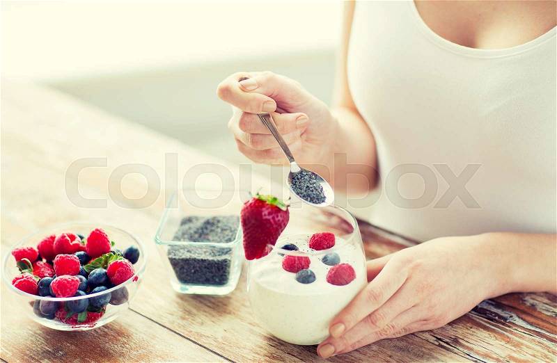 Healthy eating, vegetarian food, diet and people concept - close up of woman hands with yogurt, berries and poppy or chia seeds on spoon, stock photo