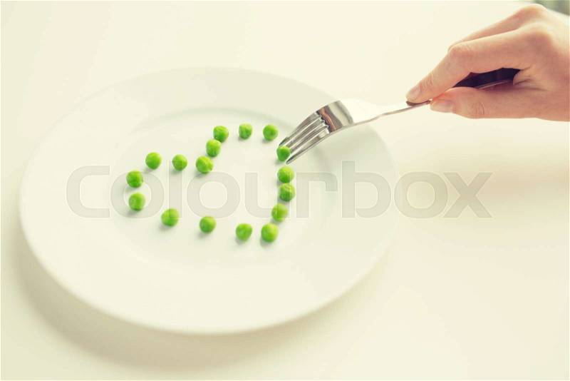 Healthy eating, dieting, vegetarian food and people concept - close up of woman with fork eating peas in shape of heart, stock photo