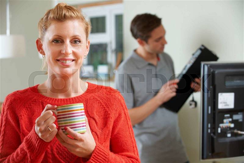 Woman Holding Mug Whilst Engineer Installs TV Equipment, stock photo