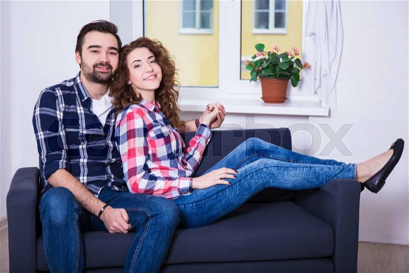 Portrait of young beautiful happy couple sitting on sofa in living room, stock photo