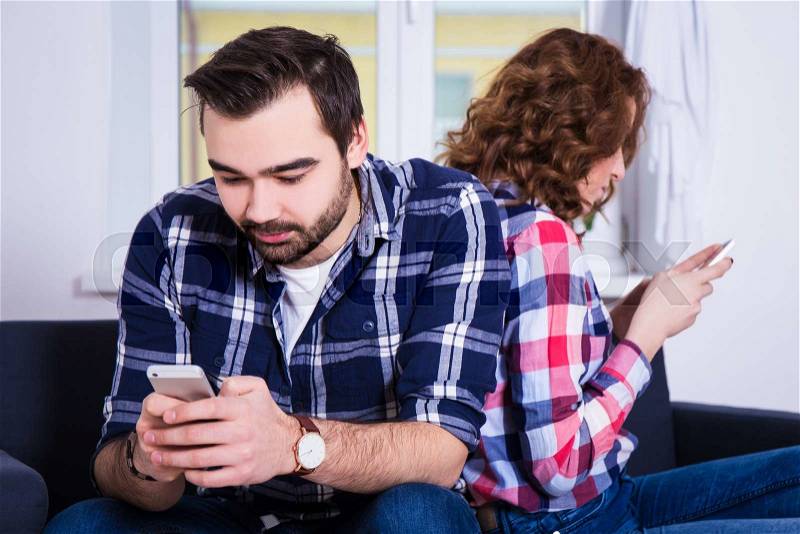 Relationship and phone addiction concept - young couple using their smart phones at home, stock photo