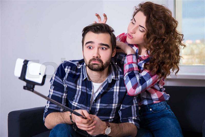 Happy funny couple taking photo with cell phone on selfie stick st home, stock photo