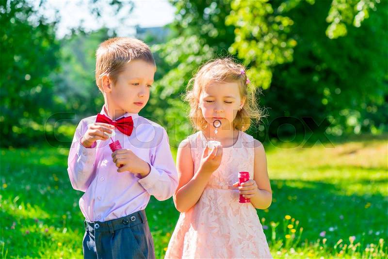 Six year old boy looks at the girl makes soap bubbles, stock photo