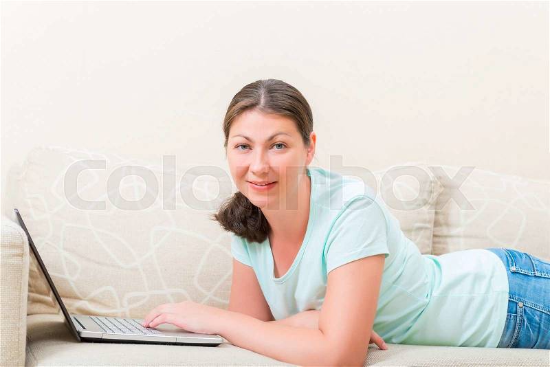 Woman with laptop lying on the couch comfortably, stock photo