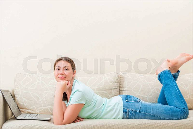 Woman at home working in the internet while lying on the couch, stock photo