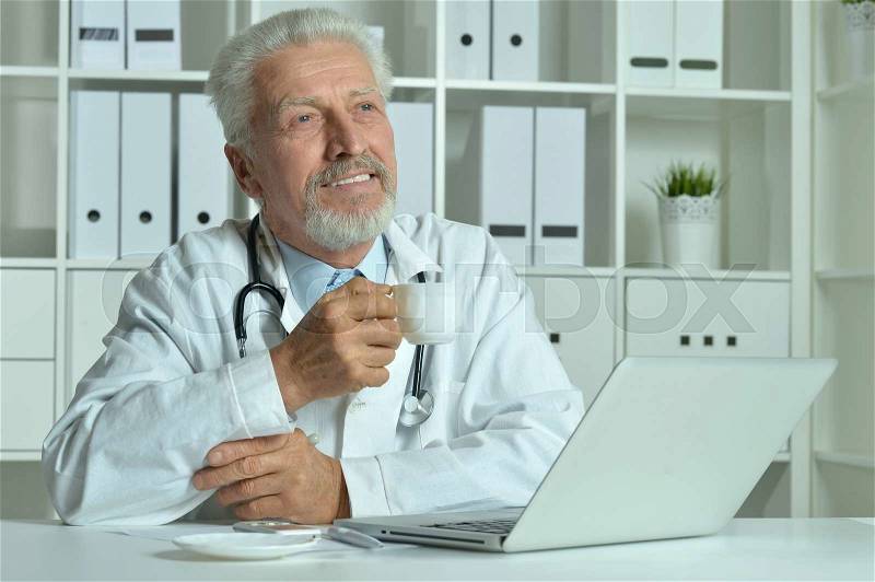 Portrait of a elderly doctor with laptop in office, stock photo