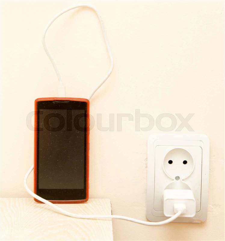 Cell phone is being charged from the electrical outlet, stock photo